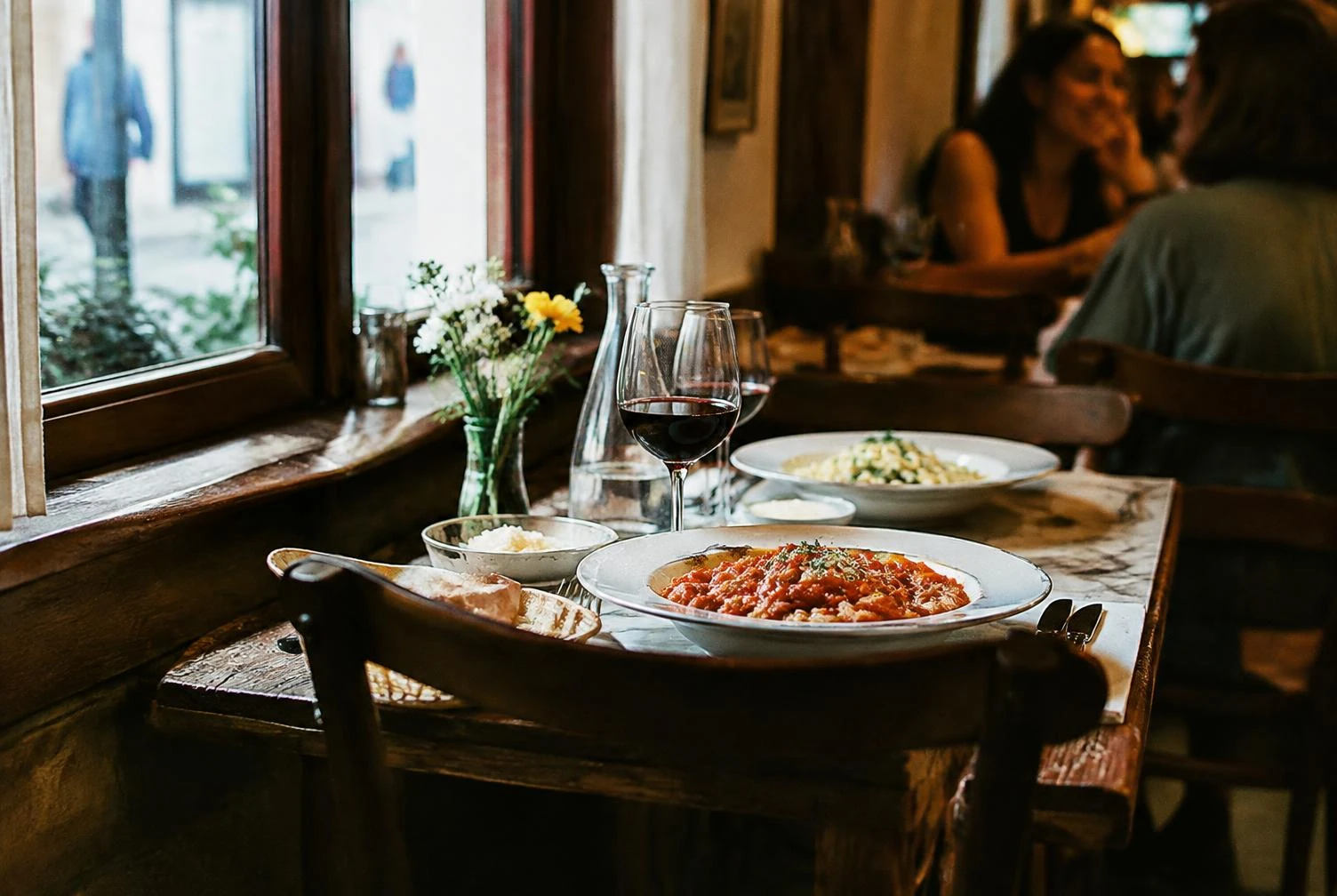 A window table in a small trattoria with pasta and red wine
